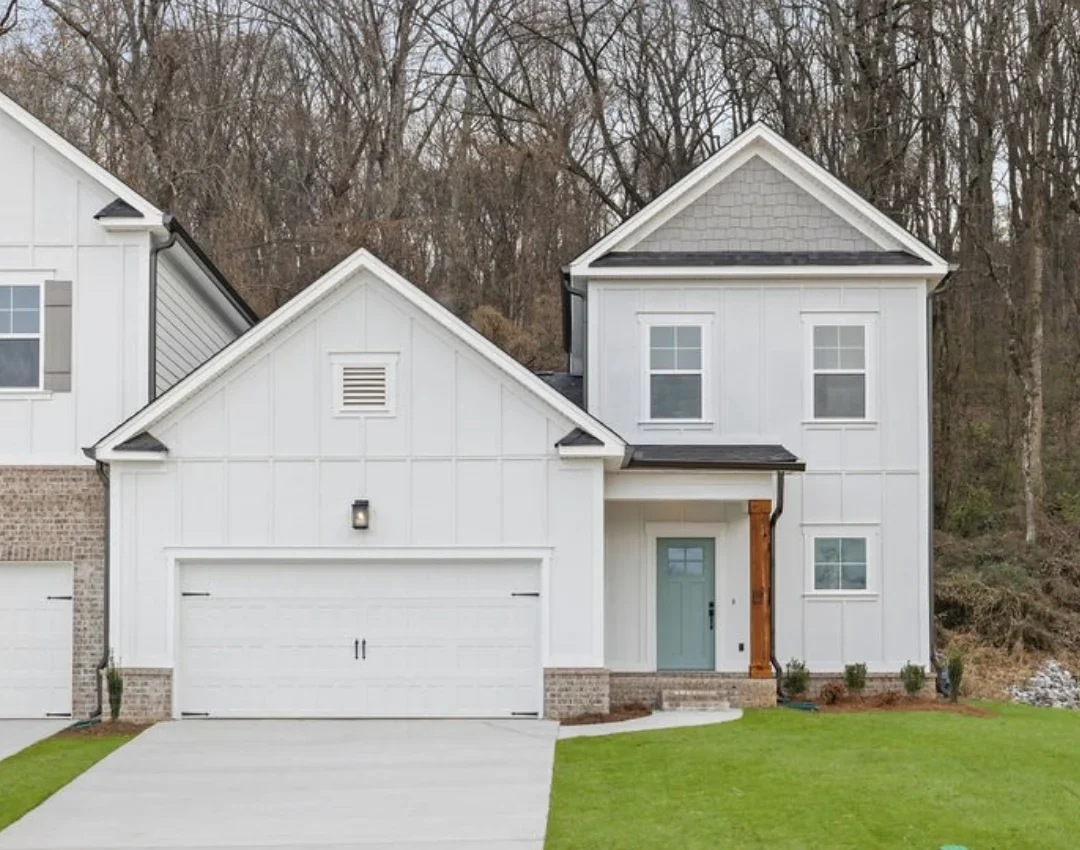 New Home Chattanooga TN. Two-story white house with gabled roof, garage, and a tidy lawn. Built by Pratt Home Builders. Forest background.