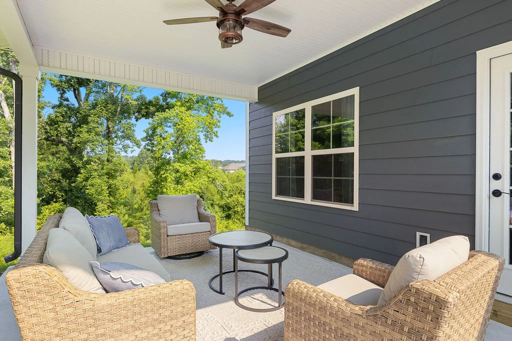 Covered patio by Pratt Home Builders in Chattanooga TN, featuring wicker furniture, a ceiling fan, and lush green views.
