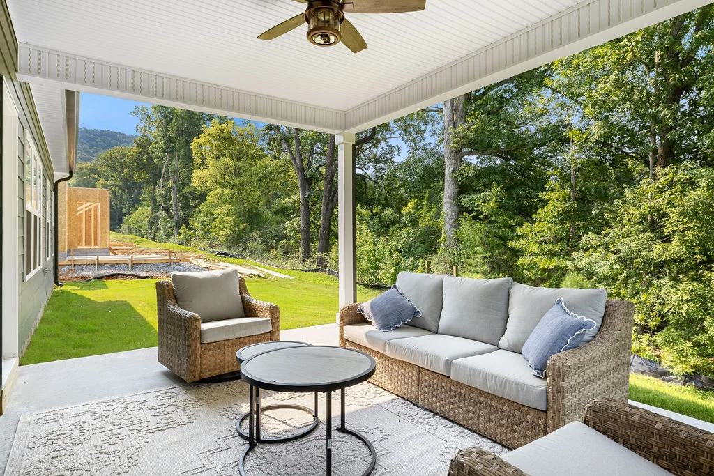 Covered patio with wicker seating, ceiling fan, and forest view at a Pratt Home Builders property in Chattanooga, TN.