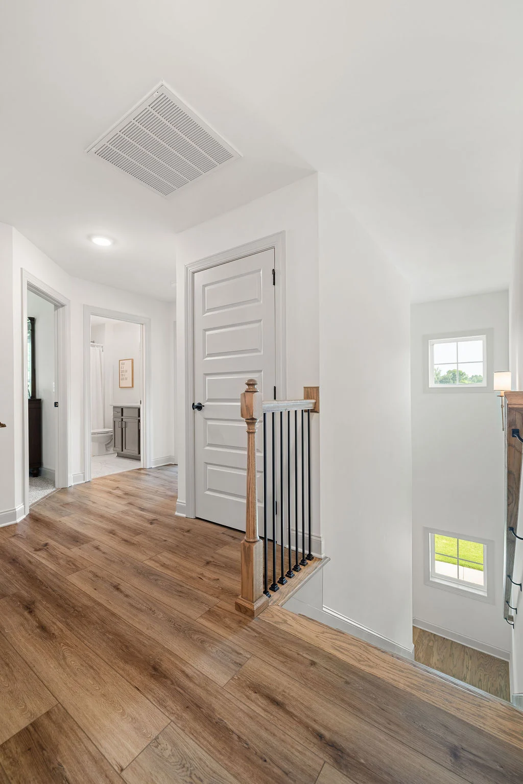 Bright hallway with wood flooring, white doors, modern railing, and bathroom access, designed by Pratt Home Builders in Chattanooga TN.