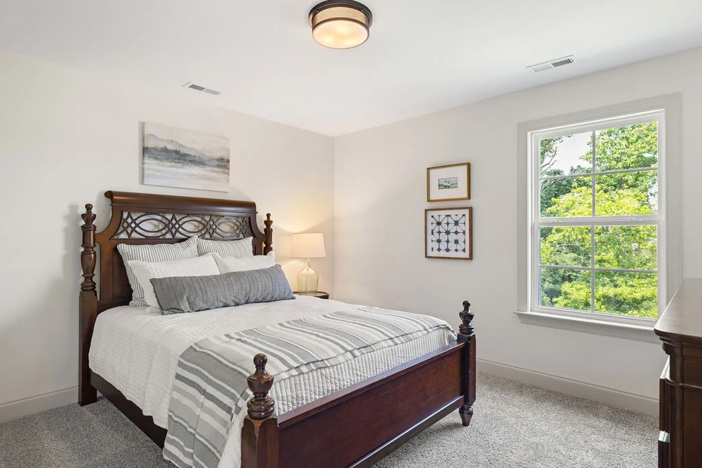 Bright bedroom with wood bed, striped bedding, framed art, and large window. Designed by Pratt Home Builders in Chattanooga TN.