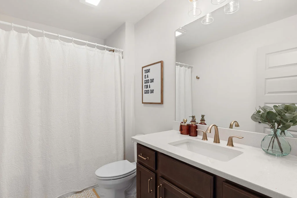 Elegant bathroom by Pratt Home Builders in Chattanooga TN, featuring dark wood vanity, gold fixtures, framed quote, and a white shower curtain.