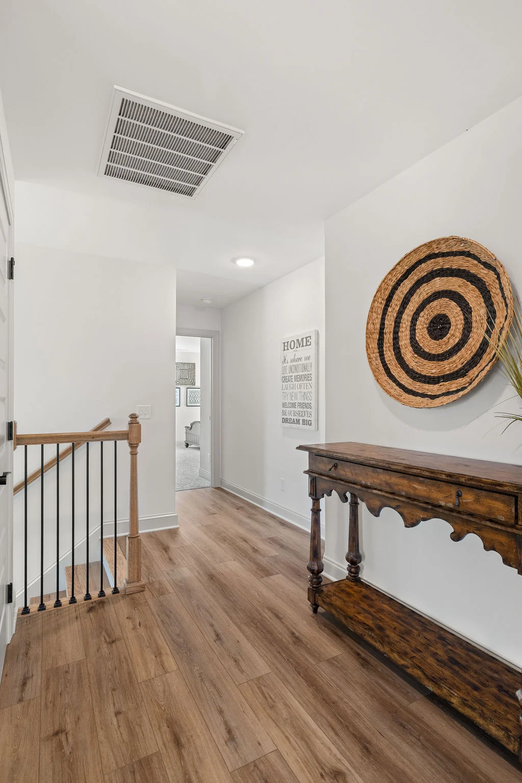 Hallway with wood flooring, decorative table, basket wall art by Pratt Home Builders in Chattanooga TN; sign with inspiring words on wall.