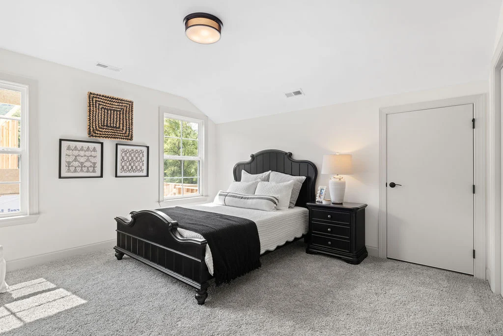 Bright bedroom featuring a black bed and nightstand, soft white bedding, and wall art by Pratt Home Builders in Chattanooga TN.