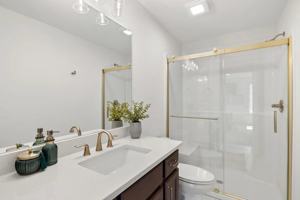 Modern bathroom with glass shower, gold fixtures, dark vanity, and decorative plants, designed by Pratt Home Builders in Chattanooga TN.