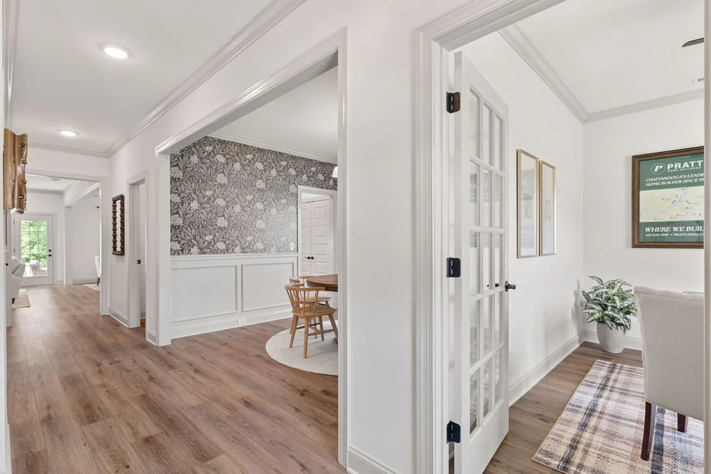 Modern hallway with wood floors, floral wallpaper, and dining area. Pratt Home Builders sign on wall; Chattanooga, TN. Bright, spacious design.