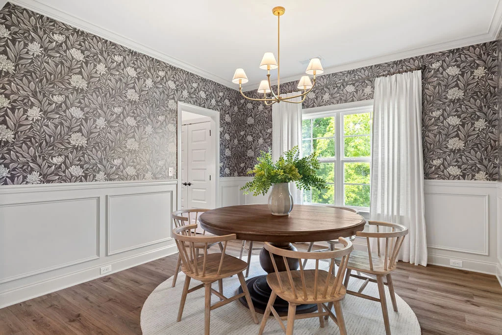 Chic dining room with floral wallpaper, round wood table, and bright windows showcasing lush greenery, created by Pratt Home Builders in Chattanooga T