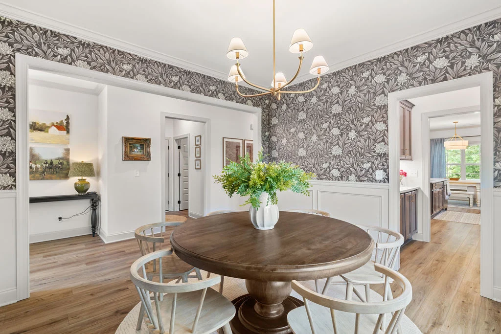 Elegant dining room by Pratt Home Builders in Chattanooga TN, featuring floral wallpaper, round wooden table, and modern chandelier.