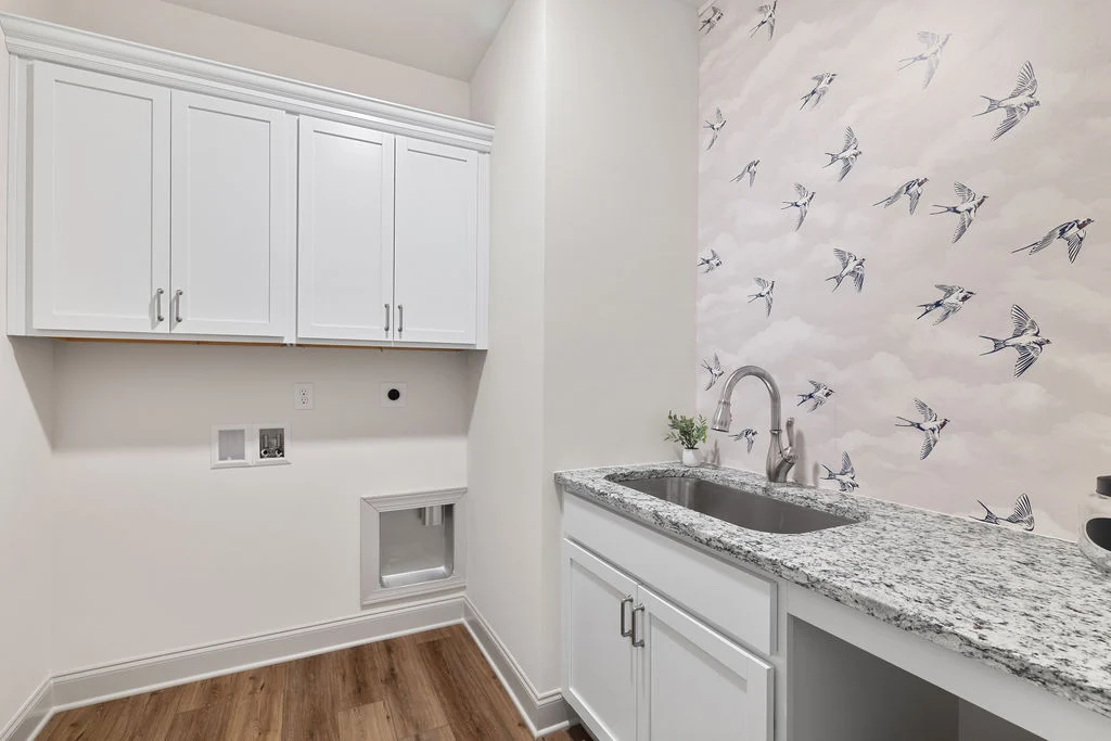 Laundry room with bird-themed wallpaper, granite countertop, and white cabinets by Pratt Home Builders in Chattanooga, TN.