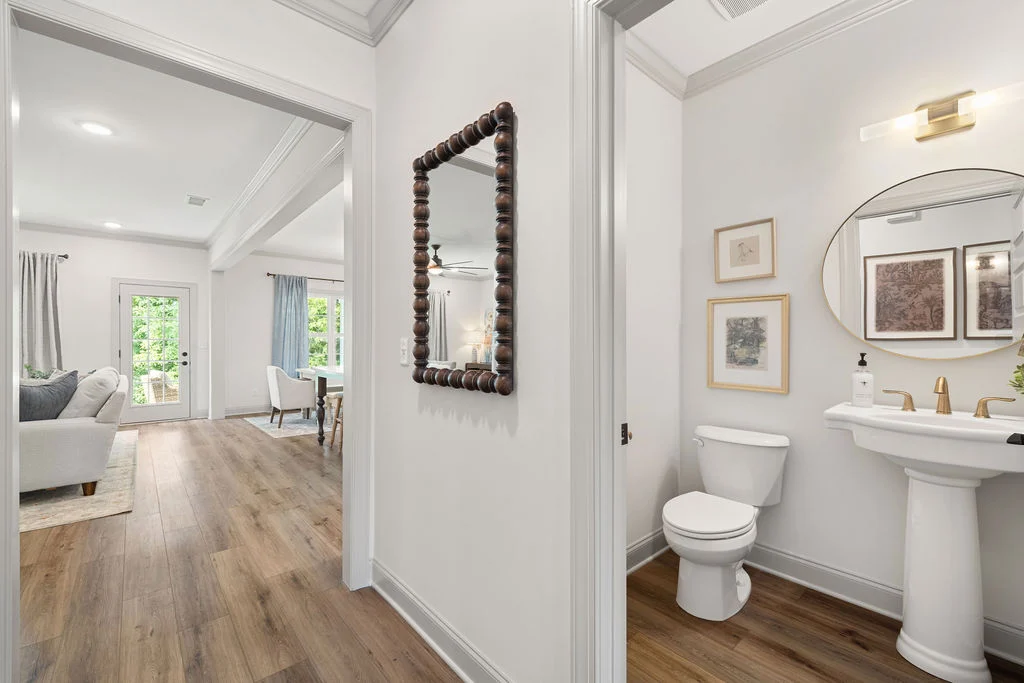 Bright hallway with wooden floors leading to a cozy living area and a modern half-bath. Design by Pratt Home Builders in Chattanooga TN.