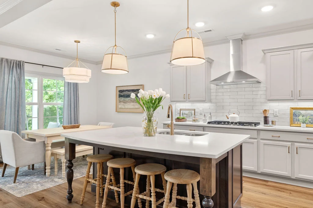 Bright kitchen by Pratt Home Builders in Chattanooga, TN, features white cabinets, island with stools, pendant lights, and dining area near window.