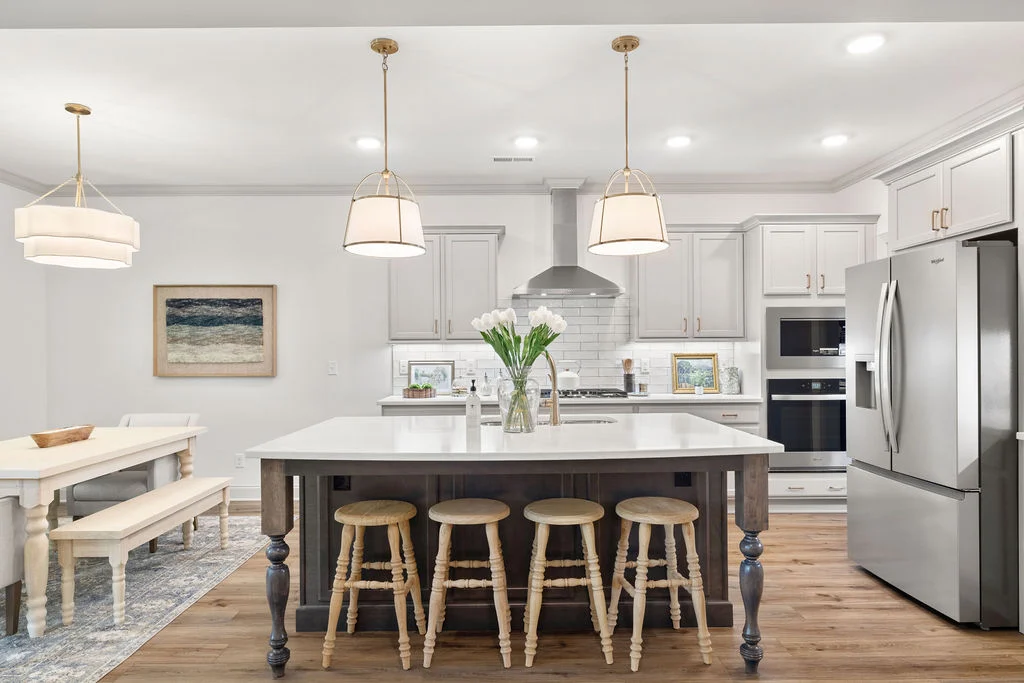 Modern kitchen with white cabinets, island with stools, stainless appliances, and pendant lights. Designed by Pratt Home Builders in Chattanooga TN.