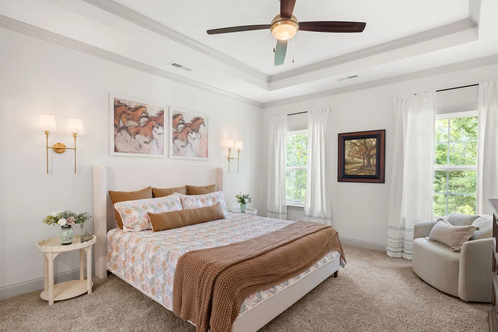 Elegant bedroom with large bed, floral bedding, and brown accents. Features a ceiling fan and artwork. Built by Pratt Home Builders in Chattanooga TN.
