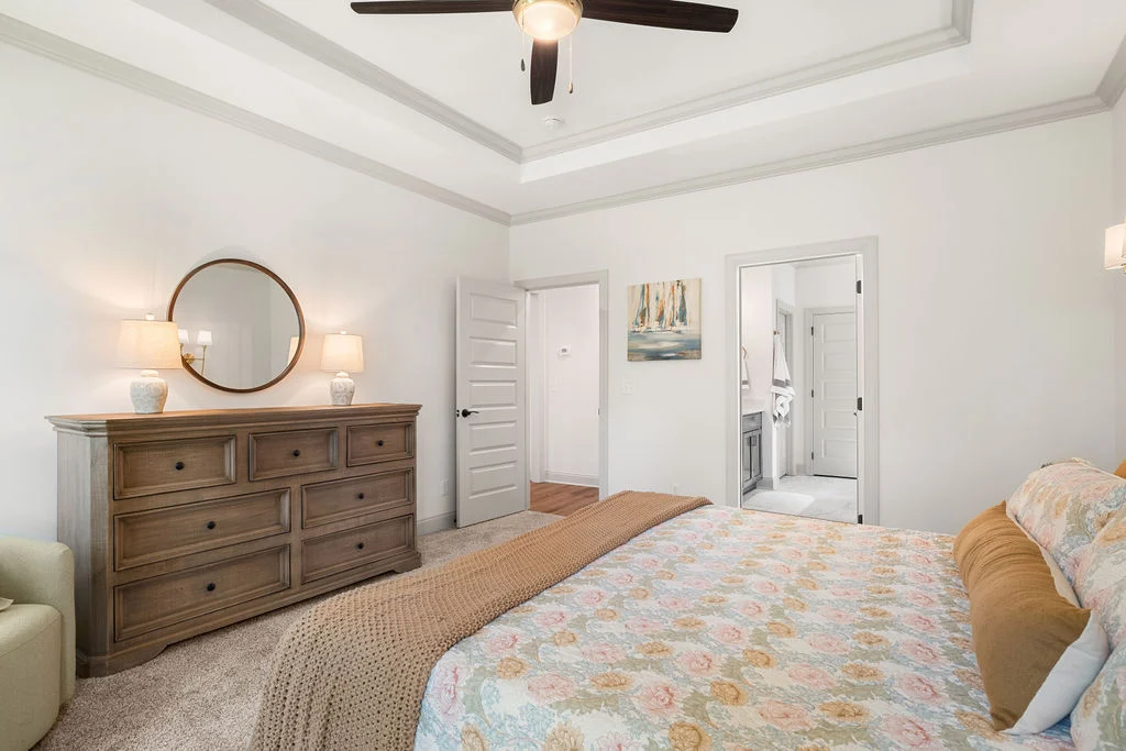 Elegant bedroom with floral bedding, wooden dresser, and ceiling fan. Decor by Pratt Home Builders in Chattanooga TN. Bathroom visible through door.