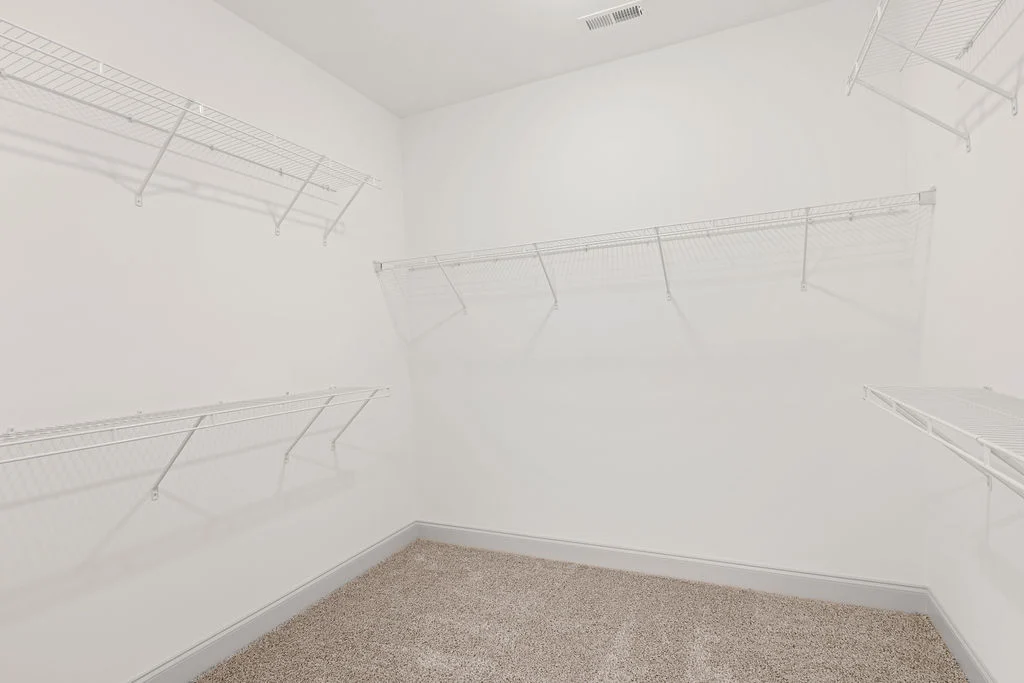 Spacious white walk-in closet with wire shelving by Pratt Home Builders in Chattanooga TN. Carpeted floor and bright lighting.