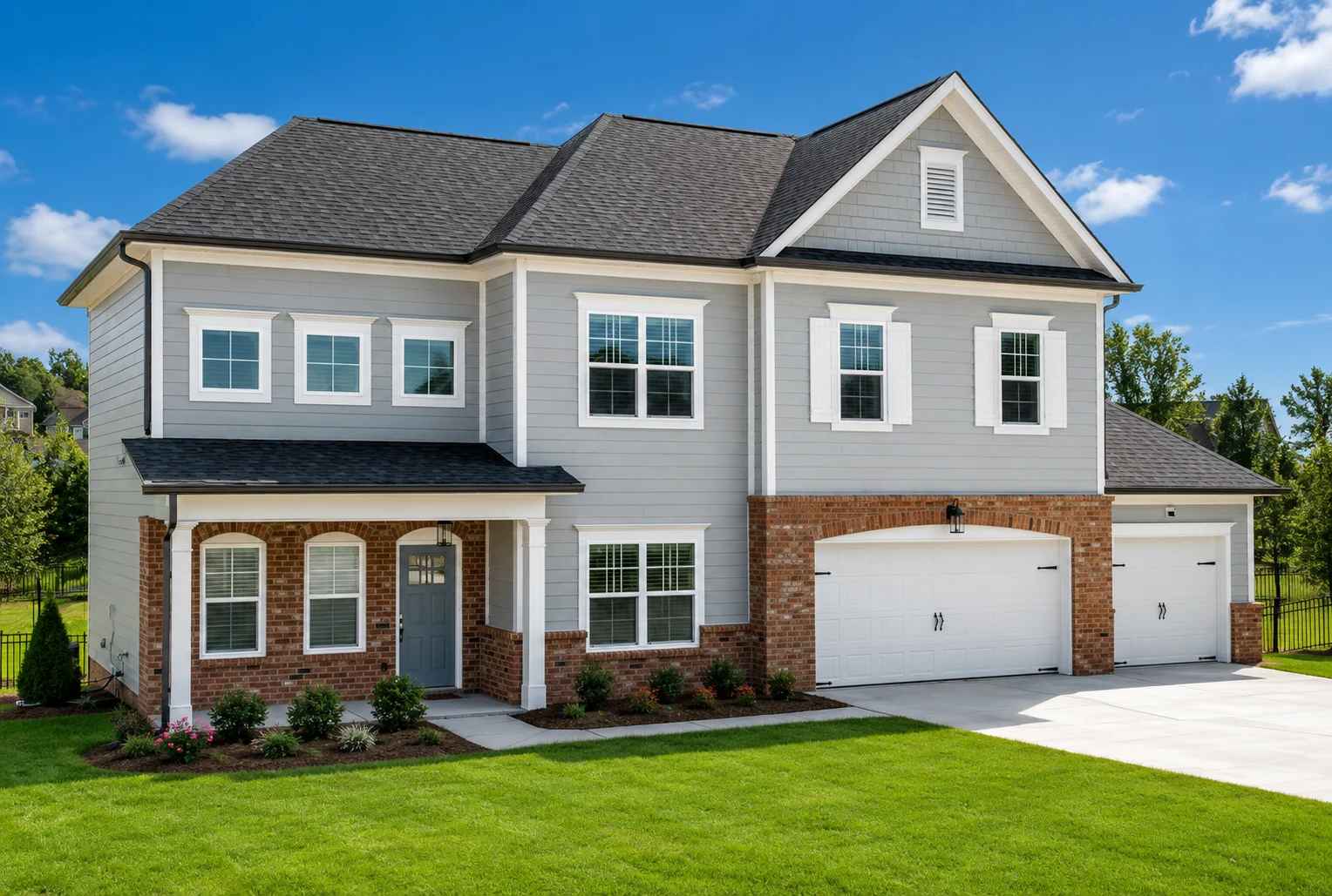 Two-story home with gray siding, brick accents, and a double garage by Pratt Home Builders in Chattanooga TN, set in a green lawn under blue sky.