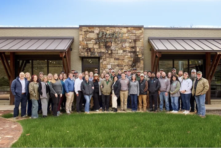 Team of Pratt Home Builders in Chattanooga, TN, standing together outside their building with stone facade and green lawn.