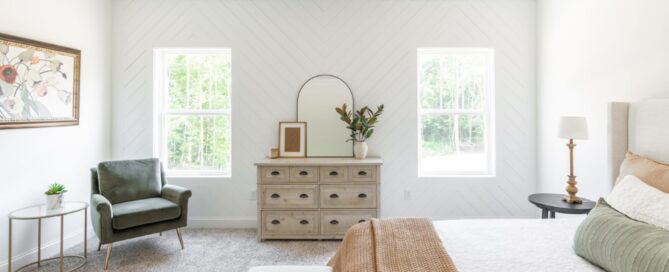 Bright bedroom by Pratt Home Builders in Chattanooga TN, featuring a green armchair, wooden dresser, and neutral bedding with natural light.