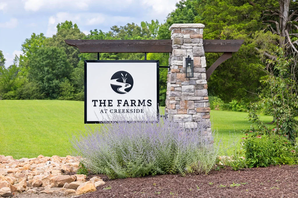 Stone entry sign with "The Farms at Creekside," surrounded by greenery. Developed by Pratt Home Builders in Chattanooga, TN.