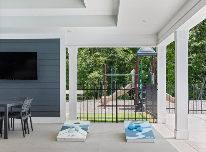 New Home Chattanooga TN. Covered outdoor area by Pratt Home Builders with cornhole boards, table, TV, and view of playground and greenery.