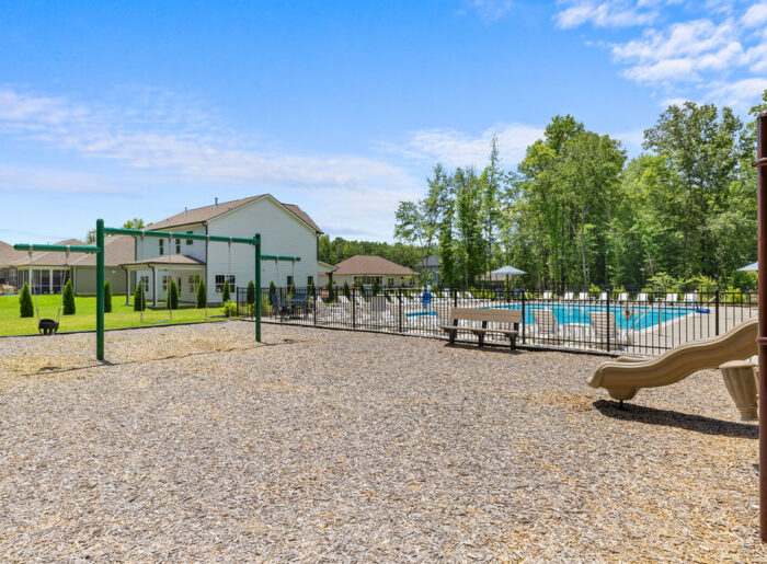 New Home Chattanooga TN. Playground with swings and slide near a fenced pool, backed by trees and homes by Pratt Home Builders.