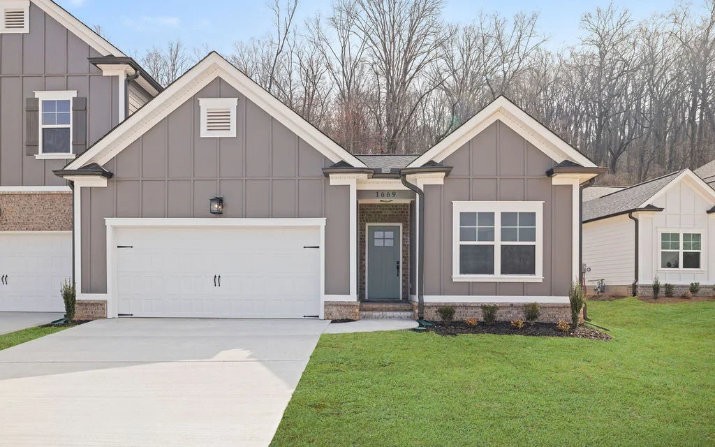 Piedmont-plan-hixson-exterior-front New Home Chattanooga TN. Single-story gray house with a double garage and manicured lawn, built by Pratt Home Builders surrounded by trees.