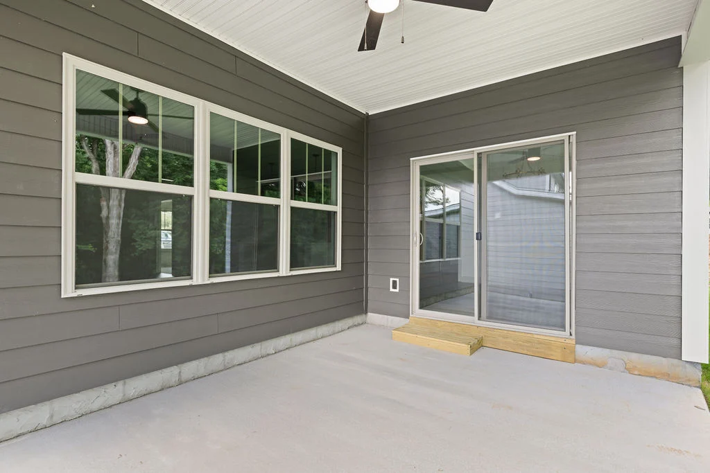 Covered patio with large windows and sliding door, featuring gray siding by Pratt Home Builders in Chattanooga TN. Ceiling fan overhead.