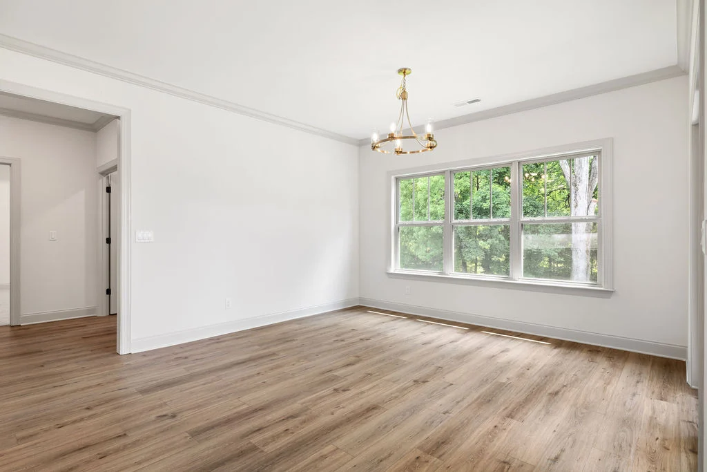 Bright, empty room with wood flooring, large window, and modern chandelier; designed by Pratt Home Builders in Chattanooga TN.