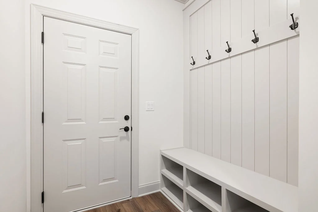 Entryway with white door, wall hooks, and storage bench. Modern and functional design by Pratt Home Builders in Chattanooga TN.