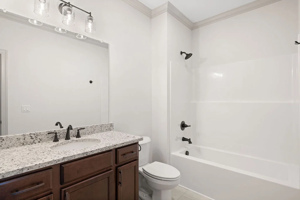 Modern bathroom with granite countertop, dark wood vanity, white bathtub, and fixtures by Pratt Home Builders in Chattanooga TN.
