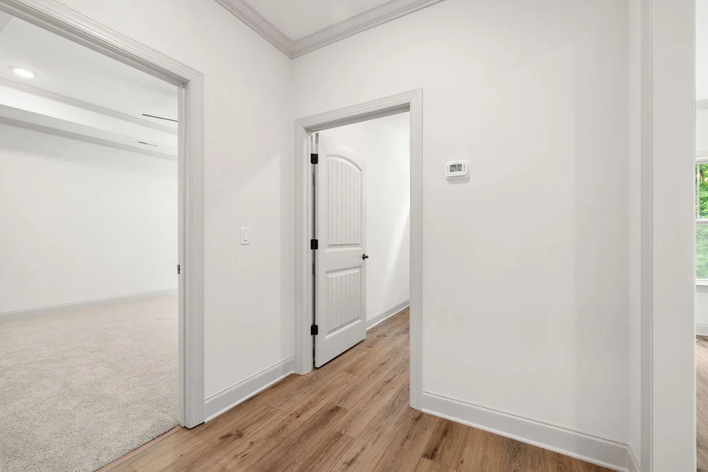 Bright hallway with wood flooring, white doors, and a visible carpeted room, crafted by Pratt Home Builders in Chattanooga TN.