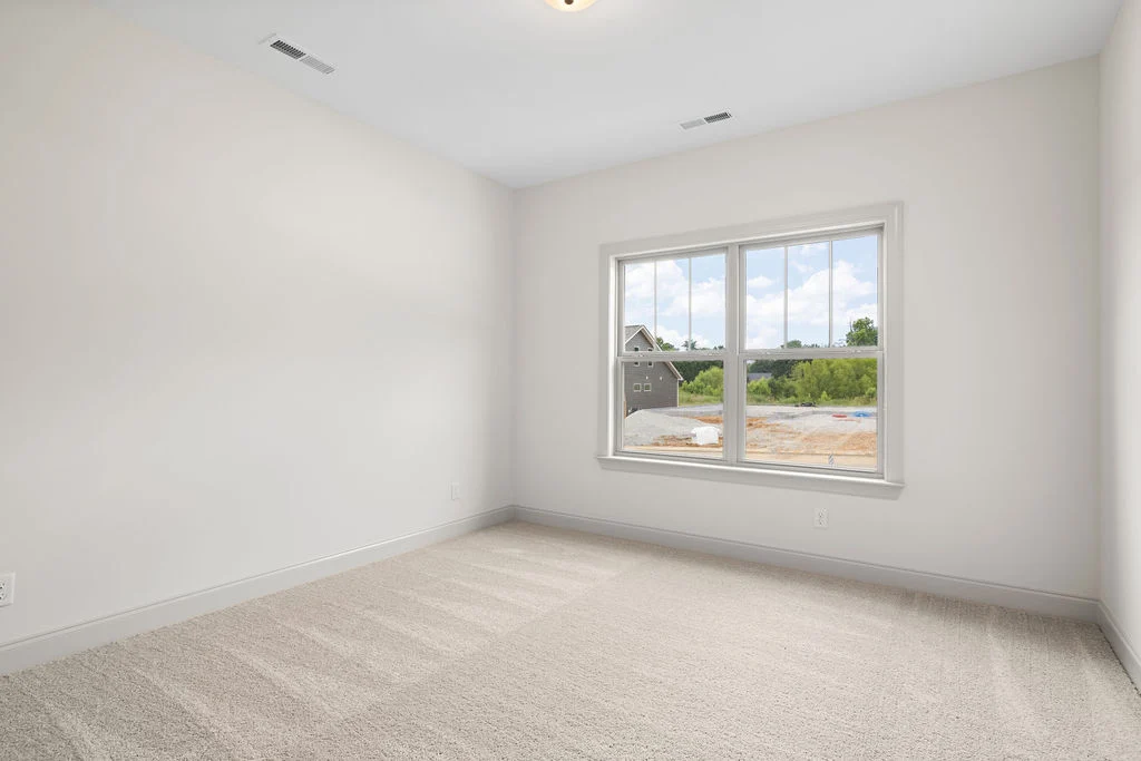Empty room with beige carpet, large window, and white walls. Construction site view. Built by Pratt Home Builders in Chattanooga TN.