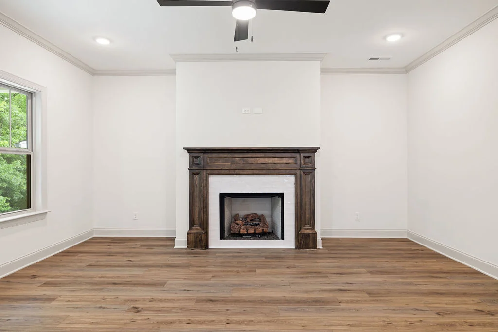 Spacious room featuring a wooden fireplace, white walls, and ceiling fan. Built by Pratt Home Builders in Chattanooga TN.