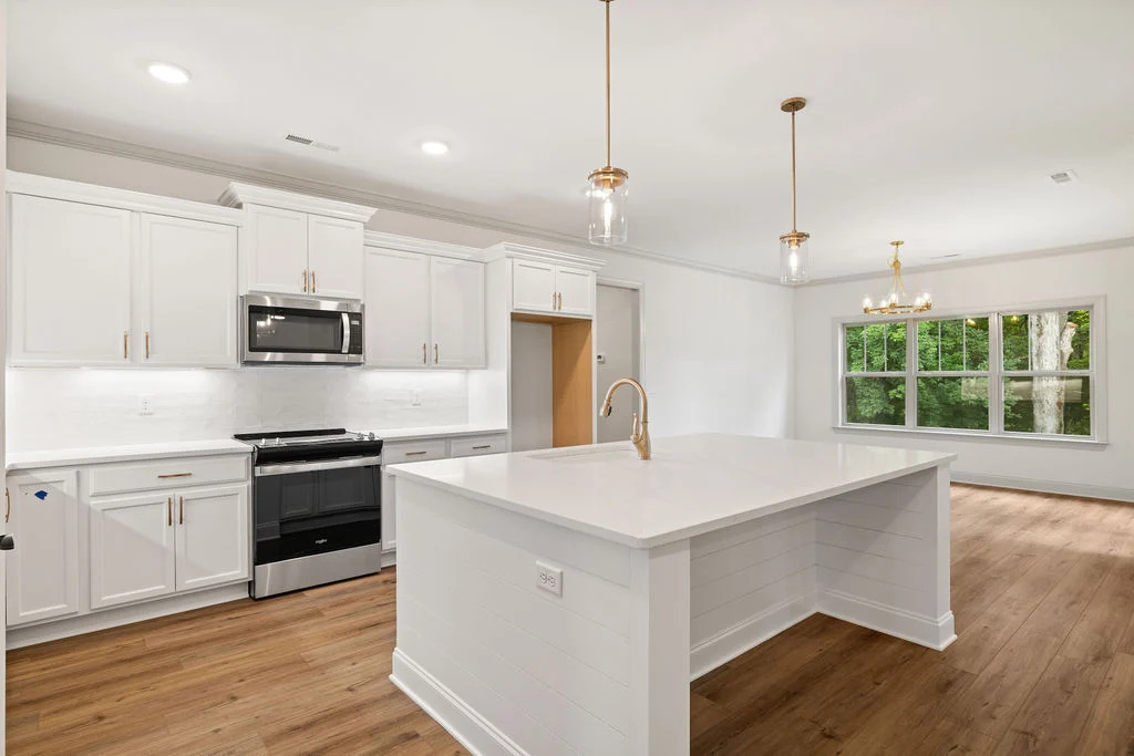 Modern kitchen with large island, white cabinetry, stainless steel appliances, and pendant lights; designed by Pratt Home Builders in Chattanooga TN.