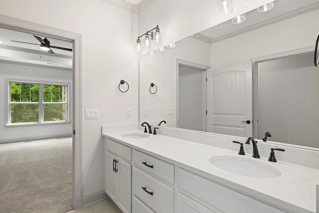 Pratt Home Builders in Chattanooga TN bathroom featuring a double vanity with black fixtures, adjacent to a bright room with a large window.