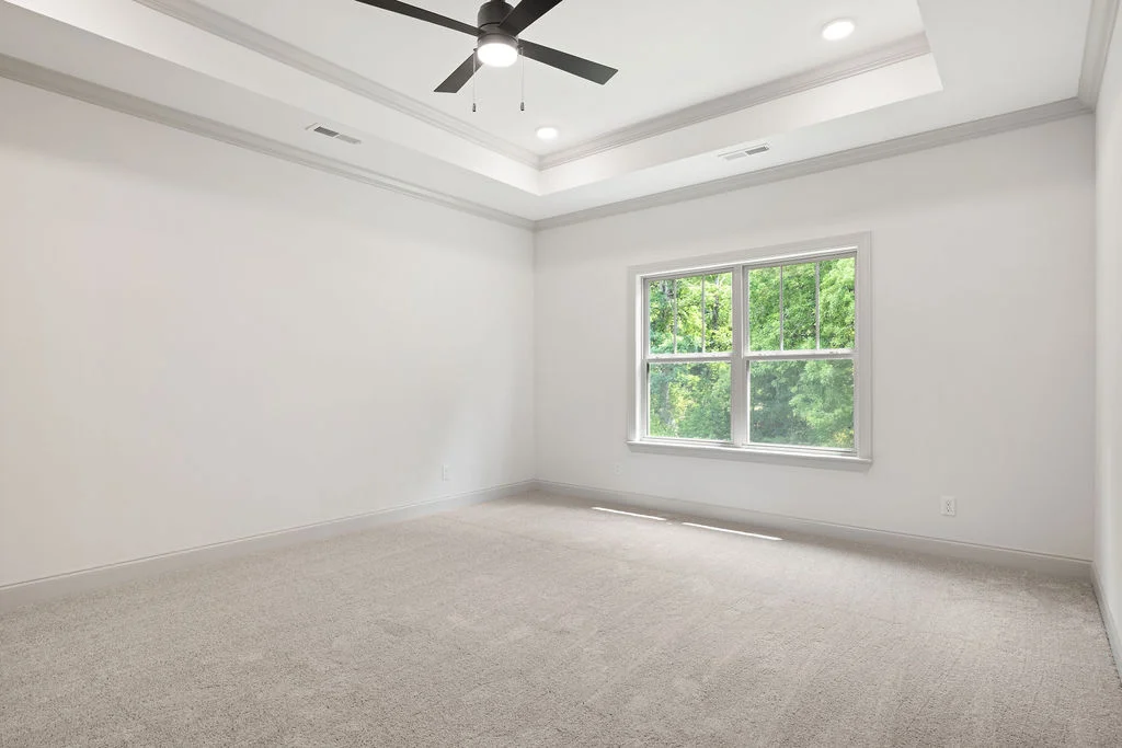 Spacious room with beige carpet, tray ceiling, and large window with green view, designed by Pratt Home Builders in Chattanooga TN.