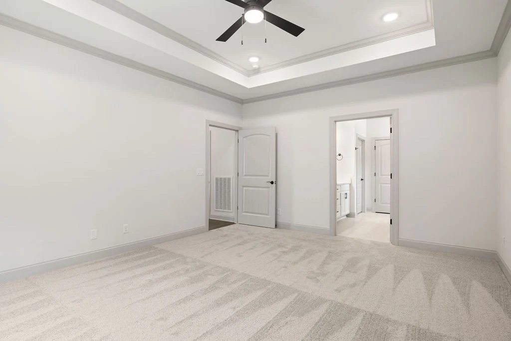 Spacious white room by Pratt Home Builders in Chattanooga TN, featuring carpeted floor, tray ceiling, recessed lighting, and two doorways.