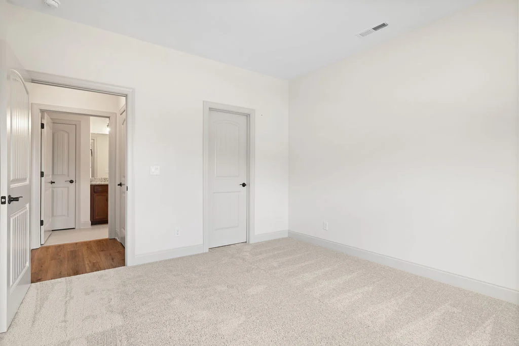 Empty beige room with carpet, two closed doors, and one open door revealing a wooden floor. Built by Pratt Home Builders in Chattanooga TN.