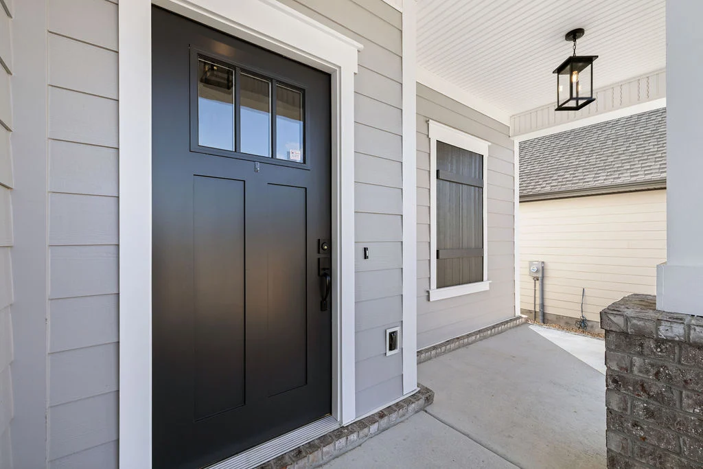 Modern entryway with a sleek black door, light gray siding, and a lantern-style fixture. Pratt Home Builders in Chattanooga TN.