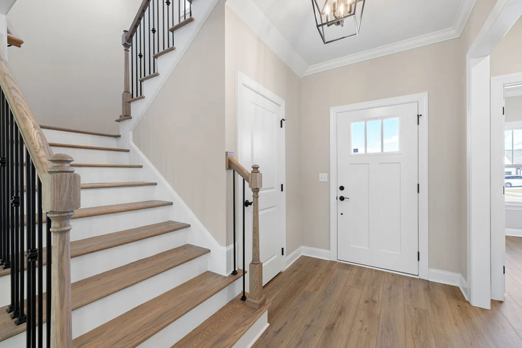 Welcoming foyer with wooden staircase, white front door, and modern light fixture. Designed by Pratt Home Builders in Chattanooga TN.