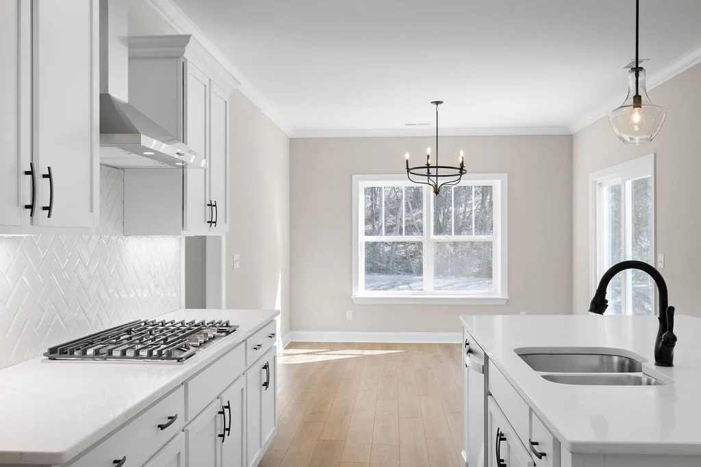 Modern kitchen with white cabinetry, island sink, and gas stove. Natural light from large windows. Built by Pratt Home Builders in Chattanooga TN.