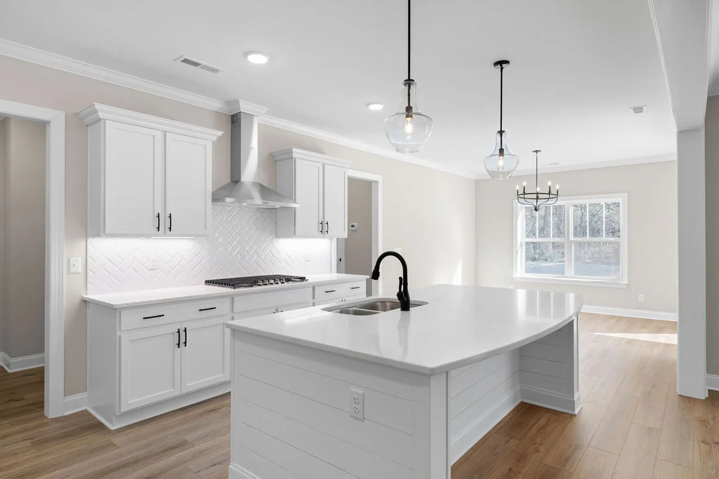 Large kitchen by Pratt Home Builders in new home now selling. in Chattanooga, TN with white cabinetry, large island, pendant lighting, and wood flooring.