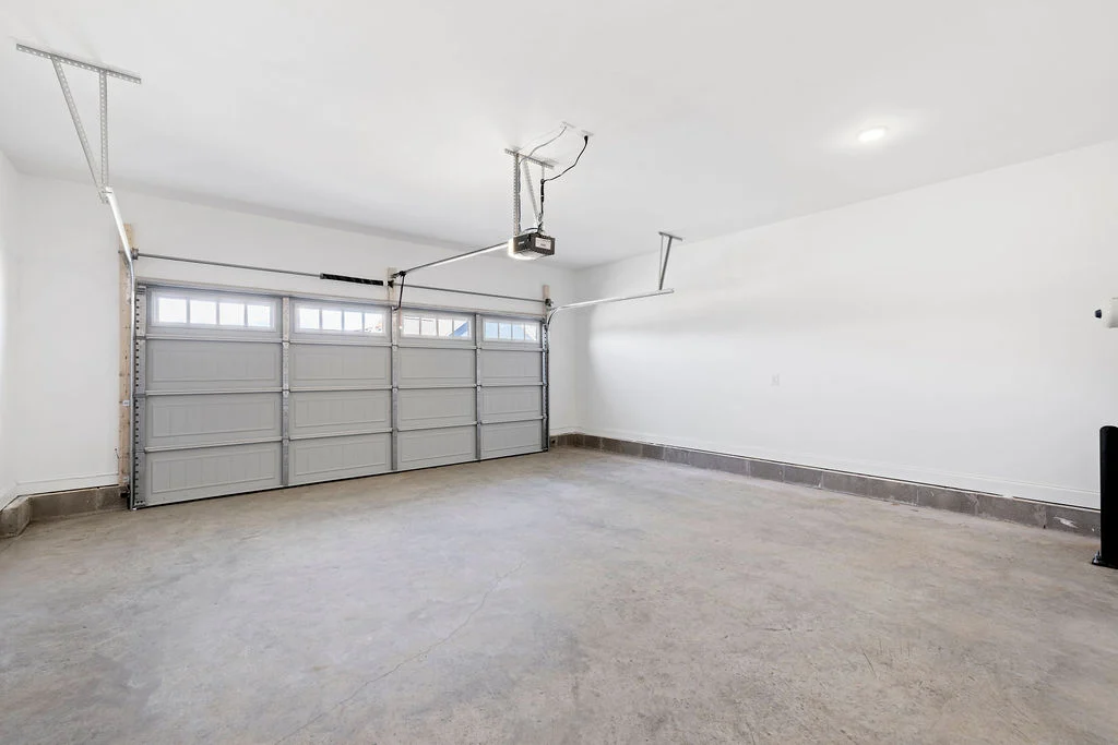 Spacious two-car garage with gray concrete floor and white walls, featuring overhead garage door openers by Pratt Home Builders in Chattanooga TN.