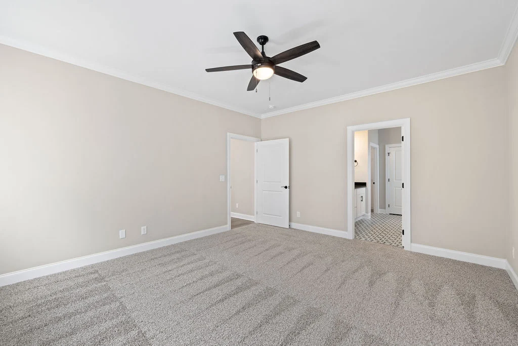 Spacious beige bedroom features carpet, ceiling fan, and access to bathroom by Pratt Home Builders in Chattanooga TN.