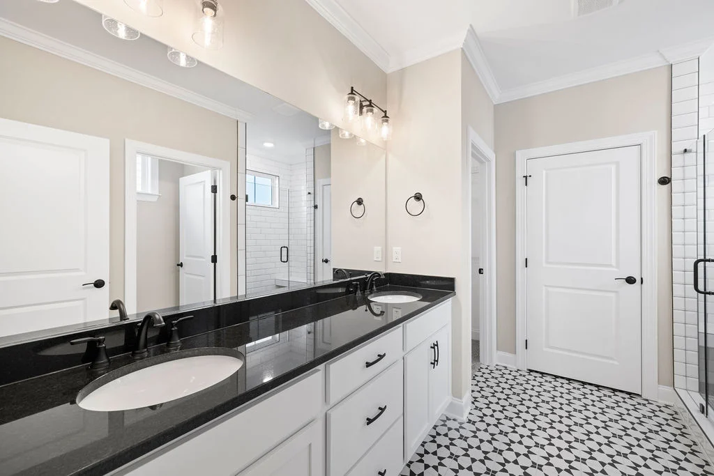 Modern bathroom with black and white decor, double sinks, glass shower, elegant lighting, and geometric tile floor by Pratt Home Builders in Chattanoo