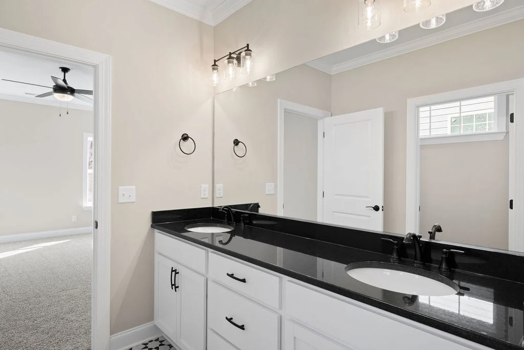 Modern bathroom with black countertop, dual sinks, large mirror, and elegant lighting. Features Pratt Home Builders in Chattanooga TN.