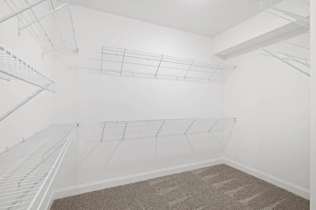 Spacious white walk-in closet with wire shelving and carpeted floor, designed by Pratt Home Builders in Chattanooga TN.
