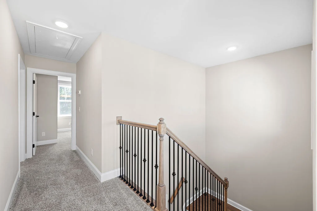 Carpeted hallway with wooden-railed staircase leading to a sunlit room, showcasing Pratt Home Builders in Chattanooga TN craftsmanship.