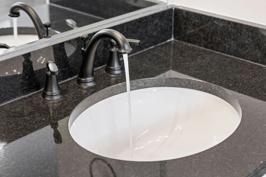 Modern bathroom sink with flowing water, set in dark granite countertop. Design by Pratt Home Builders in Chattanooga TN.