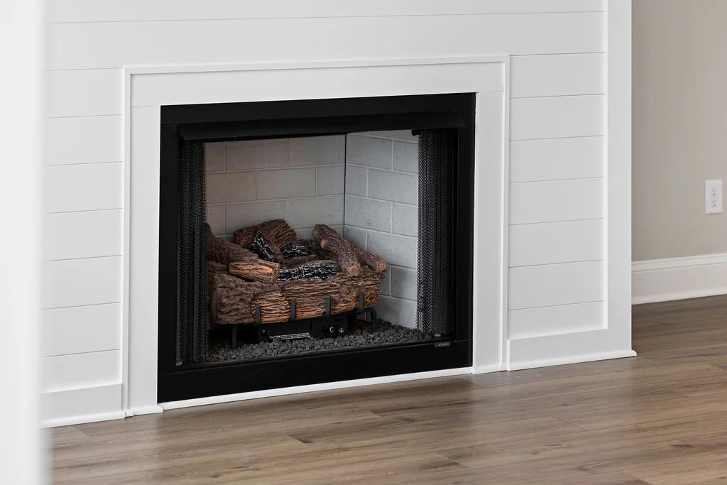 Modern fireplace with white shiplap surround, featuring realistic logs and neutral tones. Designed by Pratt Home Builders in Chattanooga TN.
